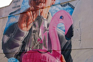 A mural of a man with sunglasses blowing up a pink inflatable flamingo.