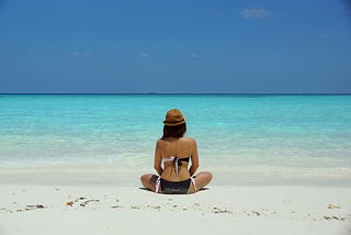 Women sitting cross-legged on beach staring out at the ocean.