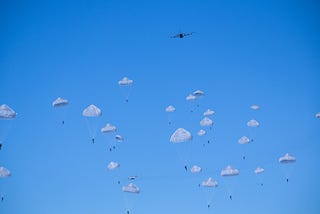 Parachutists drop from a distant plane against clear blue sky.