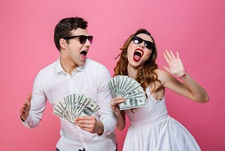 Portrait of an excited smartly dressed couple holding bunch of money banknotes and celebrating isolated over pink background