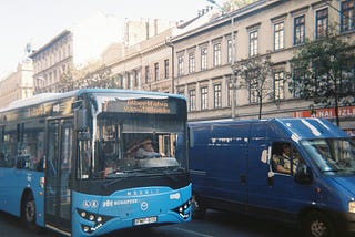 A blue bus and a blue van side by side on a street. The bus is a Budapest city bus.