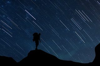 Man standing on hill at night with stars in the background.