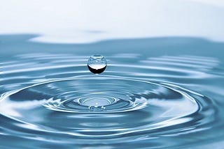 A single water droplet suspended over a body of water. Article about dehydration by Harlow Journey.