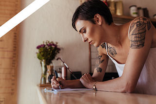 woman with arm tattoos writing at desk