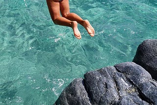 Young brunette jumping off cliff into ocean