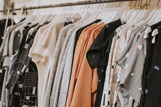 A clothing rack with shirts hung from hangers. Most grey and some orange.