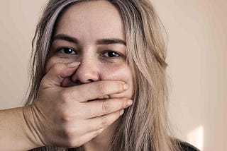 A sad, abused woman has a hand placed over her mouth to silence her.