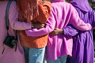 Four people seen from the back, with their arms around each other’s waists