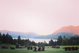 chairs on a grass hill overlooking river and surrounding hills in a pink dusk.