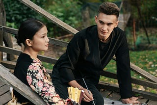 A man and a woman sitting down on a wooden bridge
