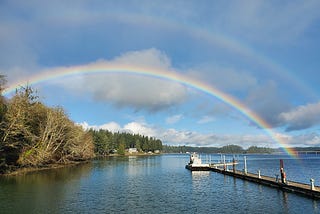 A double rainbow arches across a ship at a dock