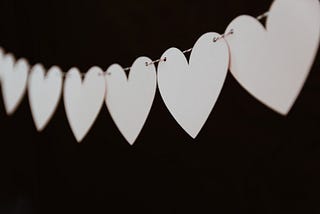 A string of white paper hearts stands out against a black background.