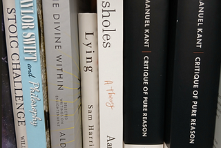 Books on a shelf including Kant’s Critique of Pure Reason, a book titled Asshole and a book titled Taylor Swift and Philosophy