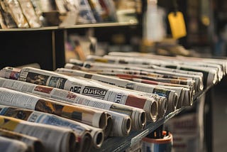 A row of neatly stacked newspapers from various publishers on display at a local stand.