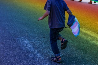 child running through a grassy field with a Trans flag in their hand