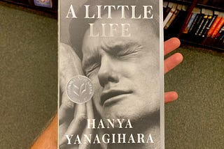 A hand holds the book A Little Life, showcasing a black and white image of a young male face in pain