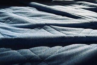 A wrinkled blue bed sheet with vividly contrasted shadows between each wrinkle.