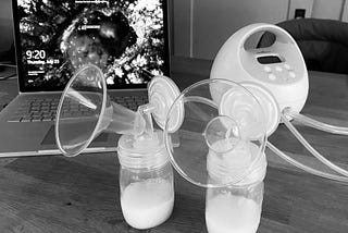 A breast pump machine sits on a desk in front of a laptop.