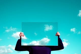 Picture of person holding up a mirror in front of their face, reflecting the sky.