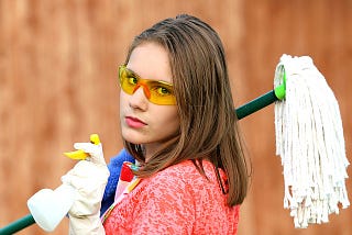 A woman holding a mop and a cleaning spray