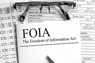 Papers on a desk with a pair of reading glasses with one of the papers reading “FOIA: The Freedom of Information Act”.