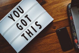 A lighted sign that says “You Got this” sits on a surface next to a smartphone.