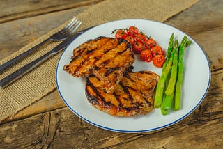 Pork chops plated with tomatoes and asparagus.