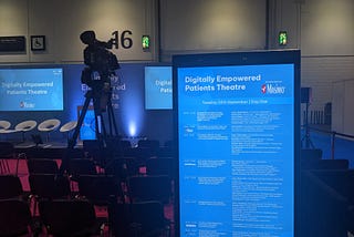 Empty stage and seating area at a conference. The stage is rather grandly named the ‘Digitally Empowered Patients Theatre’.