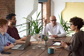 Four people sitting around a table with notebooks and computers.