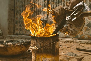 Person feeding newspaper into a dirty trashcan that is ablaze.