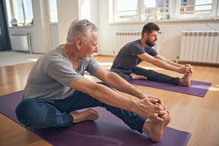 Two men on their own yoga mats, stretching.