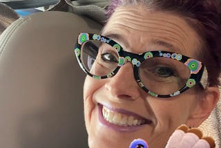 CC in a shirt with holiday lights printed on it. Her fun flowered glasses and a big smile with a Turkey sticker that says Good Vibes — This is a screenshot from the video. Scroll for video.