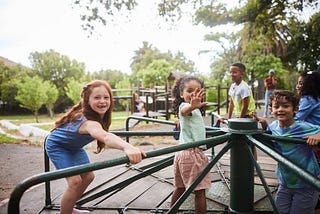 Laughing children playing on a merry-go round in a park