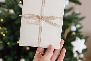 Woman’s hand holding white Christmas card against evergreen background