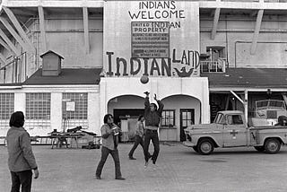 Native Americans play basketball at Alcatraz, in front of a sign that reads Indians Welcome, Indian Land.