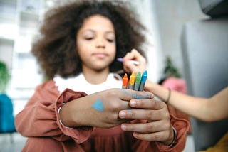 color photograph of a young child sitting and gazing lovingly at the four face painting crayons in their clasped hands