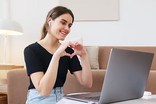 Woman in front of computer making heart shape with hands.