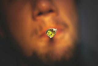A joint with the weed pronounced in the light (in a blurred guy’s mouth)
