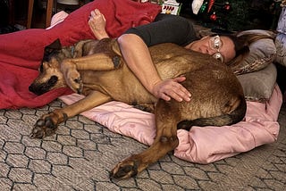 Photo of the author lying on the floor with a large dog lying beside her on a pink blanket.