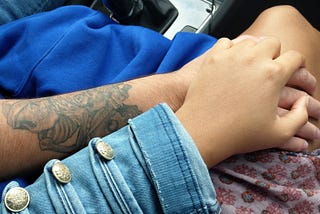 Mixed couple holding hands, man has a tatoo on his forearm.
