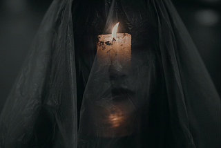 A lit candle shines through a woman’s sheer veil, casting light on her face.