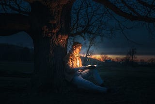 a man under the tree reading a book with a magical scene displayed.