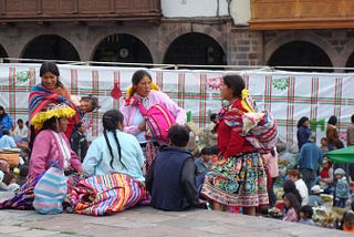 Peruvian women in colorful, traditional dress with their children at an outdoor market