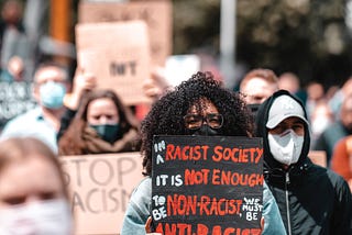 Woman holding sign that says: “In a racist society it is not enough to be non-racist, we must be anti-racist.”