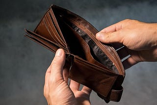 Hands of a person opening a brown leather wallet and finding it empty. Image by Andrew Khoroshavin from Pixabay.