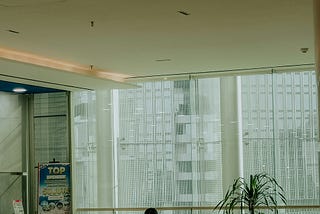 Person sitting alone in a large empty lobby, head down, surrounded by space