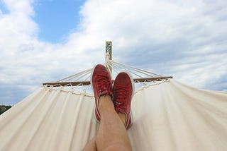 man-relaxing-in-hammock-with-red-sneakers-blue-cloudy-skies