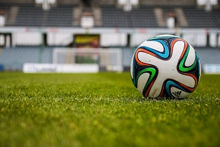 A soccer ball on a field with stands behind