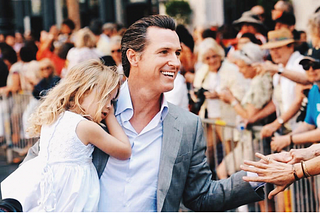 Governor Gavin Newsom of California greets voters while carrying his daughter in the times before COVID.
