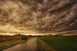 A dramatic image of a road leading towards a dark foreboding sky